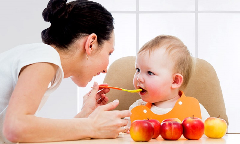 Мама кормит малыша с ложечки фруктовым пюре