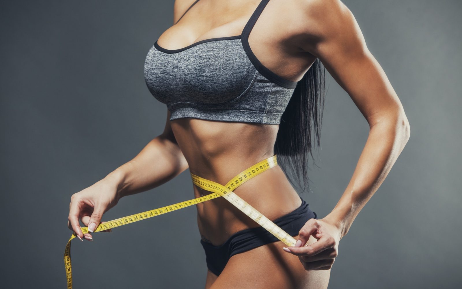 Спортивная девушка с плоским животом измеряет сантиметровой лентой свою стройную талию