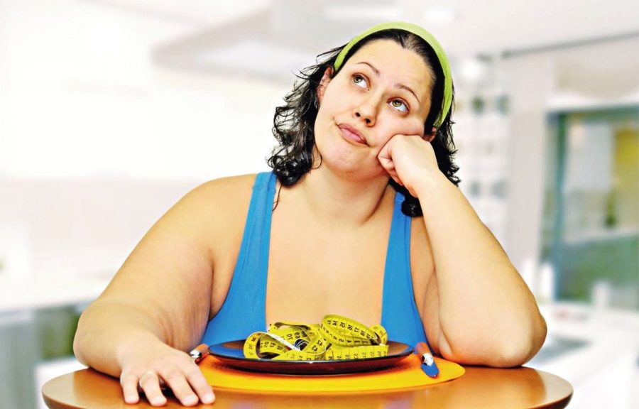 Полная девушка смотрит в потолок за столом с тарелкой еды