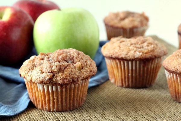 apple cinnamon muffins displayed in front of green and red apples with a blue cloth napkin